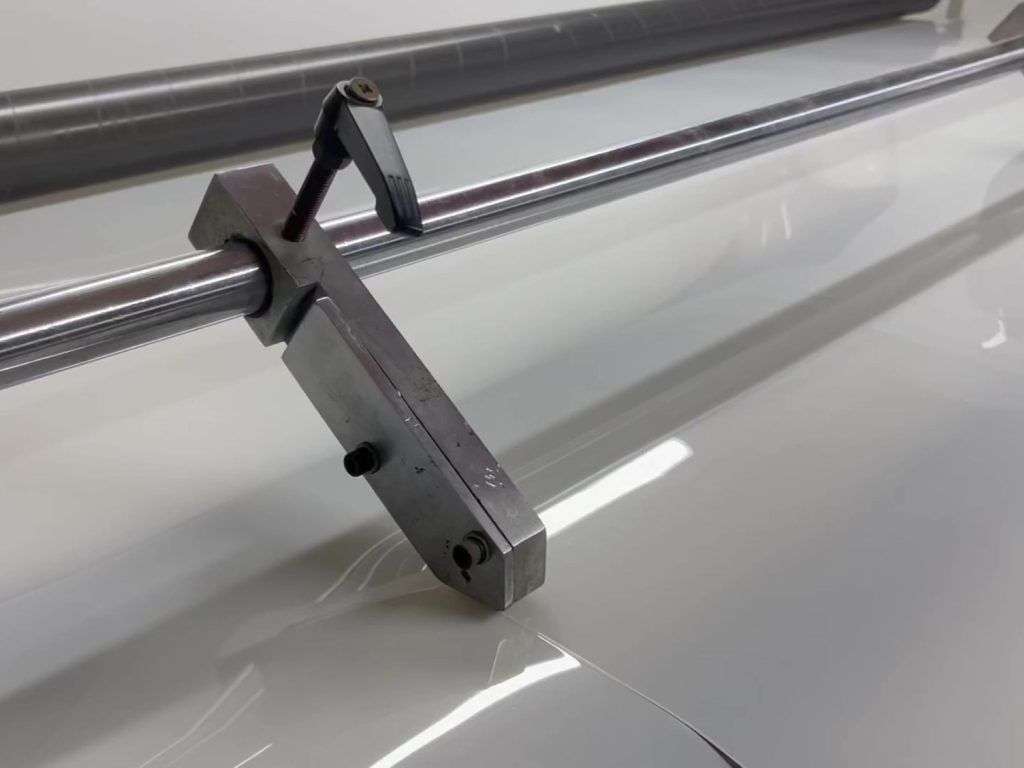 Close-up view of a metal adjustment clamp on a conveyor belt manufacturing machine.